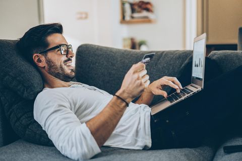 Amazon Sterne-Shop: Mann liegt mit Kreditkarte und Laptop auf einem Sofa