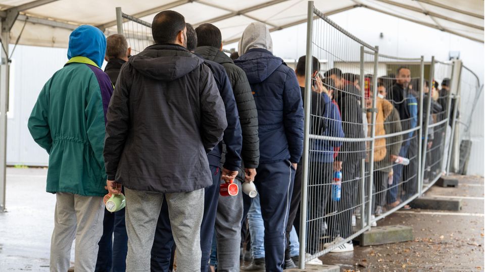 Asylbewerber und Flüchtlinge stehen vor einer Essensausgabe Schlange