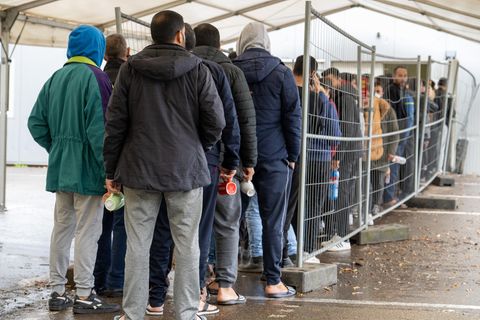 Asylbewerber und Flüchtlinge stehen vor einer Essensausgabe Schlange