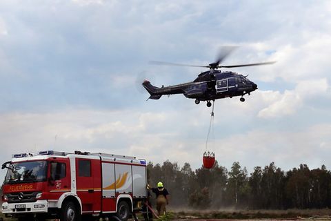 Ein Hubschrauber hebt nahe Jüterbog mit einem Wassersack neben einem Feuerwehrwagen ab