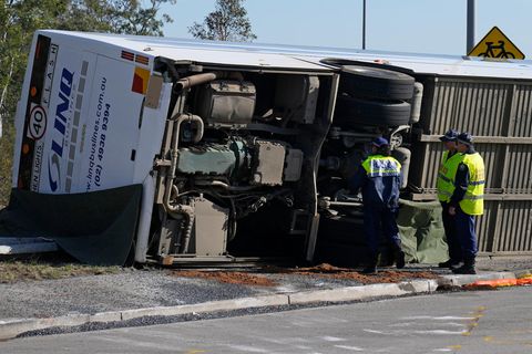 Drei Menschen mit gelben Warnwesten inspizieren die Hinterachse eines auf die linke Seite gekippten Reisebusses