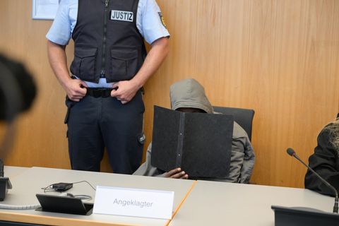 Der Angeklagte sitzt im Gerichtssaal mit eine Mappe vor dem Gesicht auf seinem Platz
