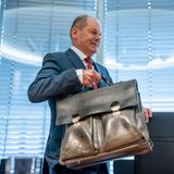 Olaf Scholz trägt seine Aktentasche und nimmt Platz