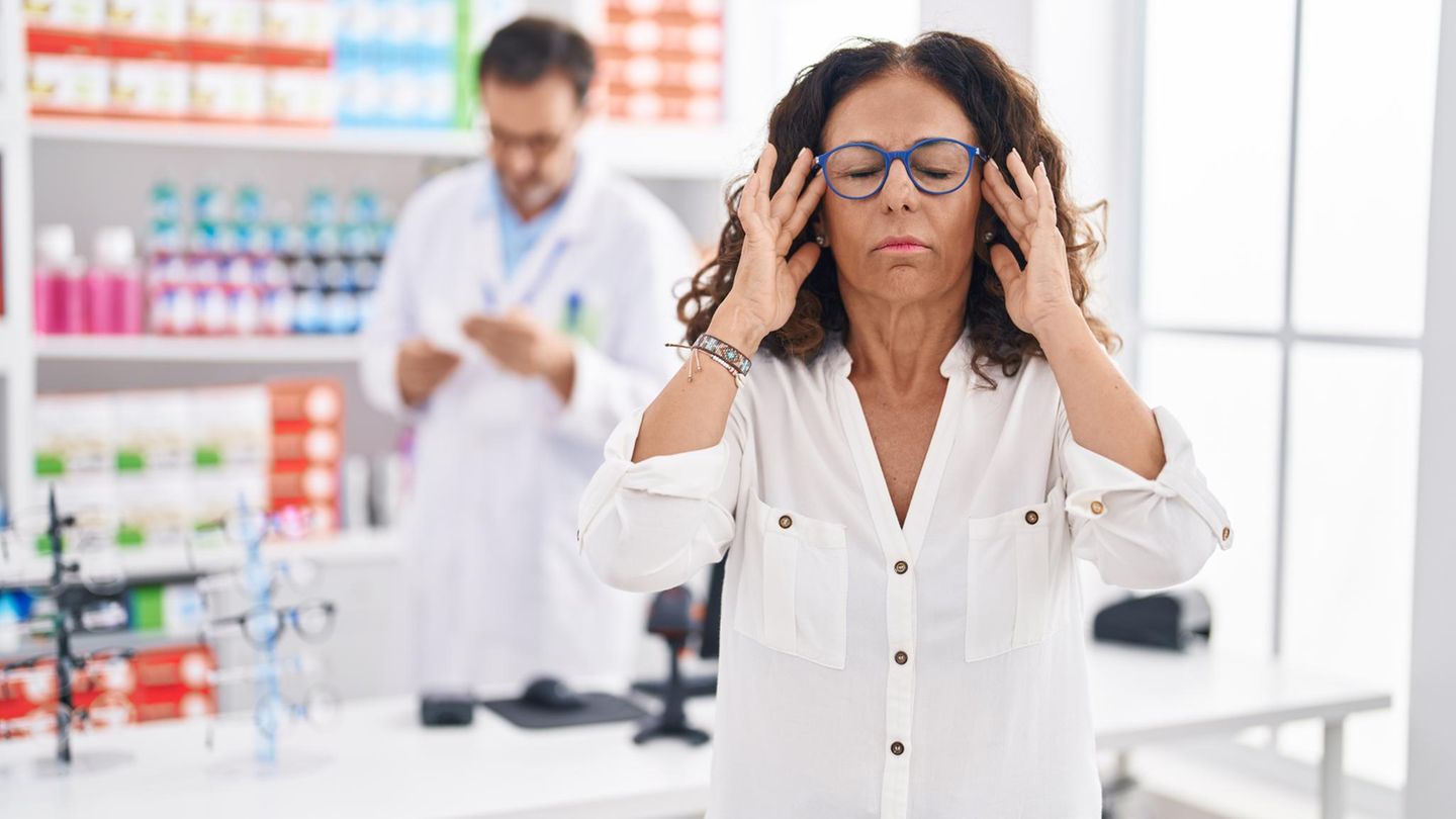 Apothekerin hält sich die Hände an die Schläfen und wirkt gestresst