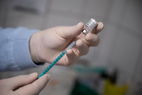Hände in medizinischen Gummihandschuhen ziehen eine Spritze mit Corona-Impfstoff auf