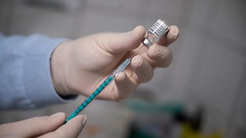 Hände in medizinischen Gummihandschuhen ziehen eine Spritze mit Corona-Impfstoff auf