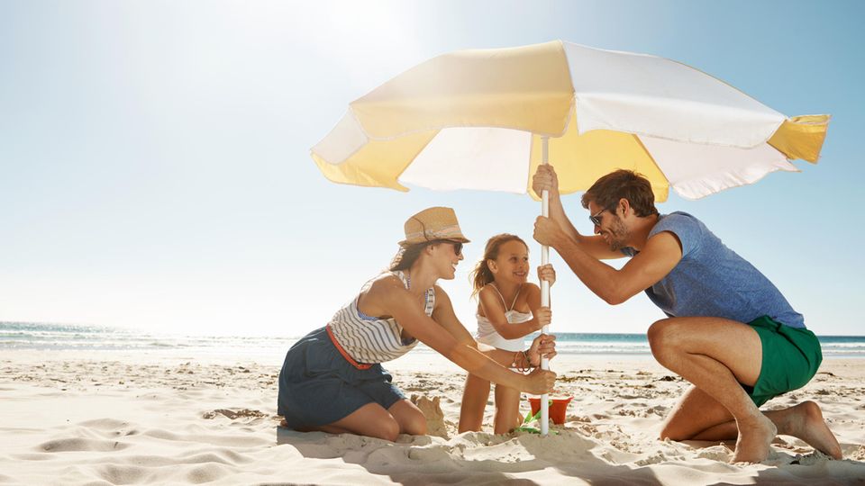 Sonnenschirm Strand: Eine Familie stellt einen Sonnenschirm am Strand auf.