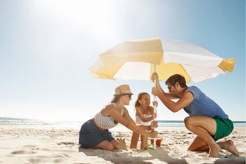 Sonnenschirm Strand: Eine Familie stellt einen Sonnenschirm am Strand auf.