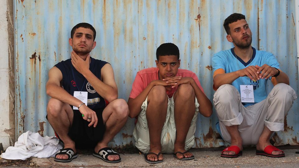 Drei Männer hocken nebeneinander auf dem Boden. Es sind Überlebende des Bootsunglücks in Griechenland