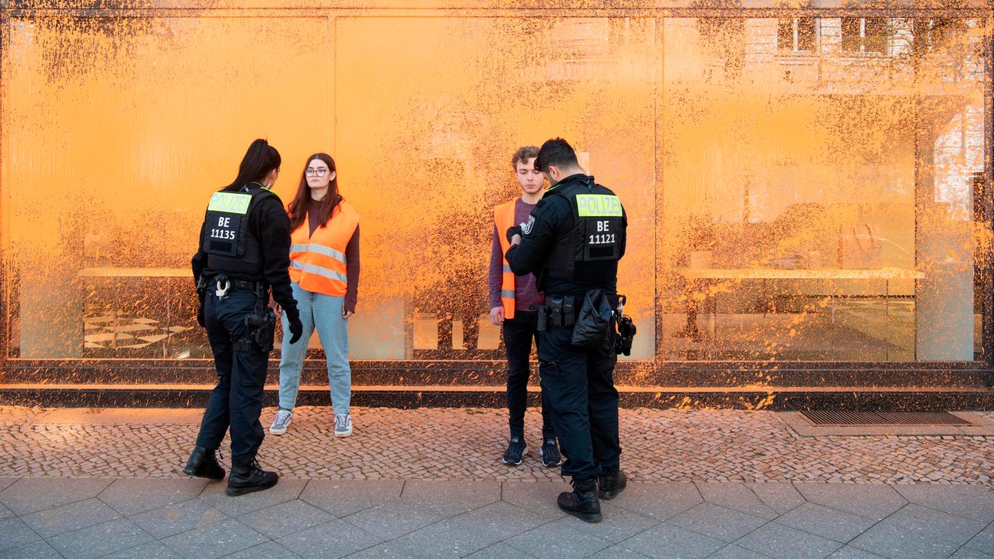 Polizisten kontrollieren Aktivisten vor farbbesprühten Schaufenstern eines Geschäfts