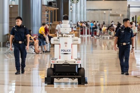 Polizisten patrouillieren an Seite des Roboters am Flughafen von Singapur