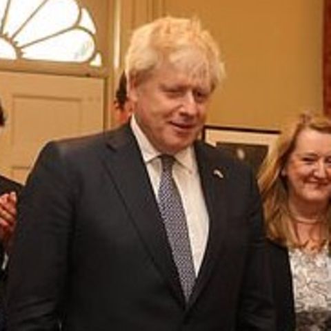 Boris Johnson steht in der Mitte eines Raumes, um ihn herum viele andere Männer und Frauen, die applaudieren