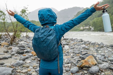 Wasserdichter Rucksack: Frau steht in Regenjacke und mit Rucksack an einem Fluss