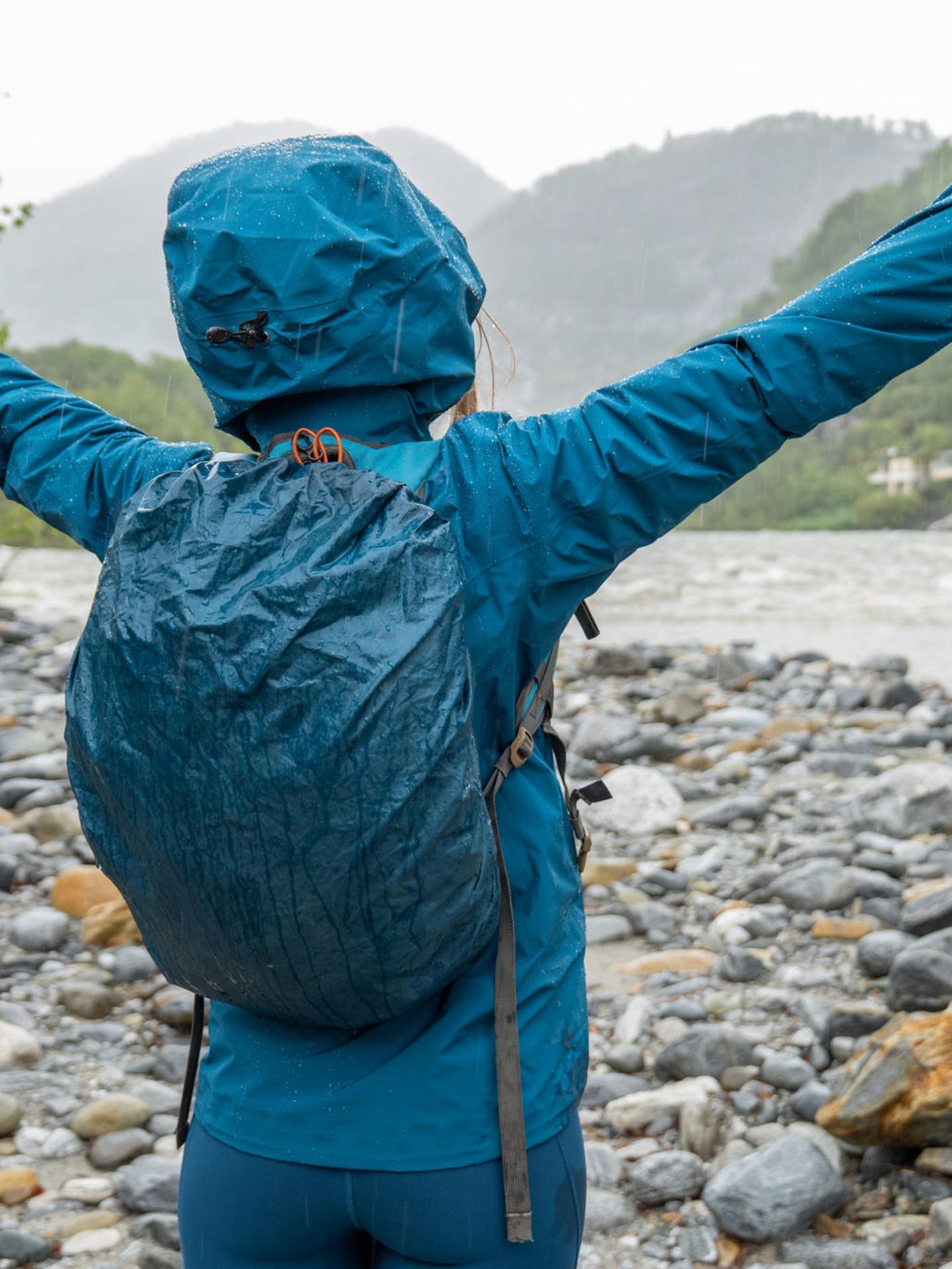 Wasserdichter Rucksack: Frau steht in Regenjacke und mit Rucksack an einem Fluss