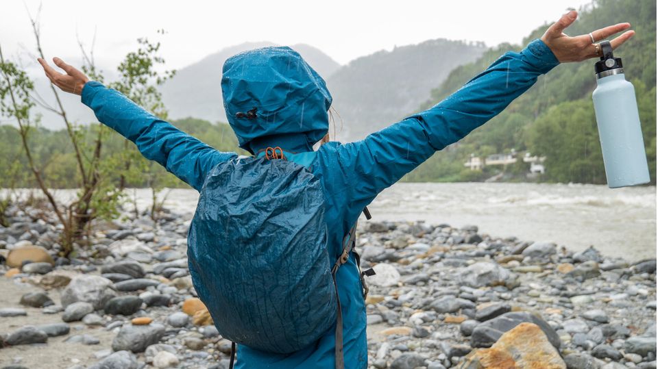Wasserdichter Rucksack: Frau steht in Regenjacke und mit Rucksack an einem Fluss