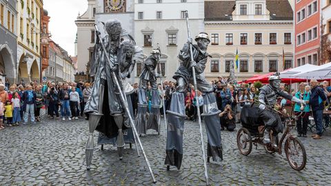 Drei Stelzenartisten laufen in Silber gekleidet über einen Marktplatz