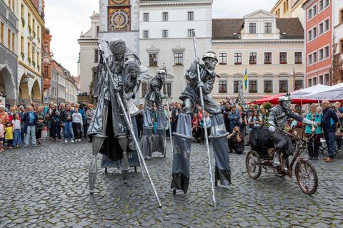 Drei Stelzenartisten laufen in Silber gekleidet über einen Marktplatz