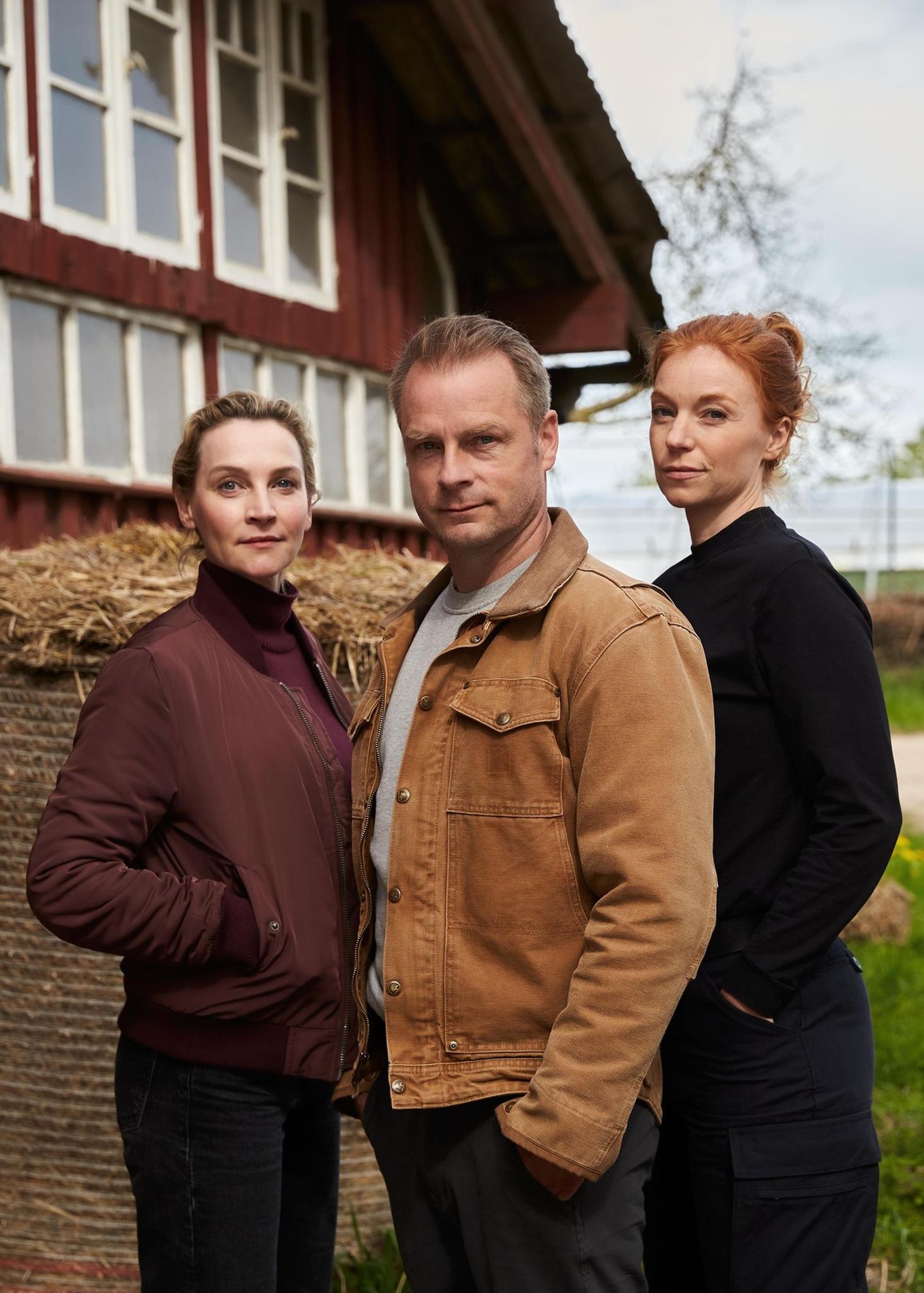 Drei Schauspieler:innen posieren vor einer Scheune