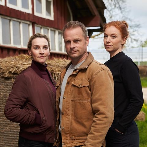Drei Schauspieler:innen posieren vor einer Scheune