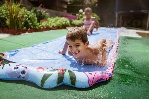 Wasserbahn für Kinder: Junge rutscht mit seiner Schwester eine Wasserbahn entlang