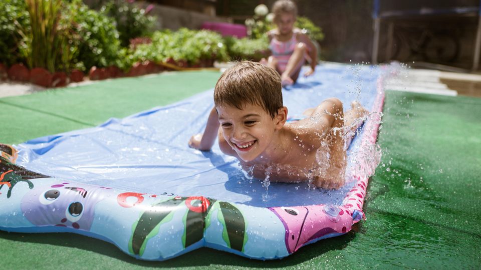 Wasserbahn für Kinder: Junge rutscht mit seiner Schwester eine Wasserbahn entlang