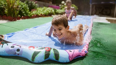 Wasserbahn für Kinder: Junge rutscht mit seiner Schwester eine Wasserbahn entlang