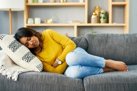 PMDS: Eine Frau liegt auf dem Sofa, hat Schmerzen und hält sich den Bauch