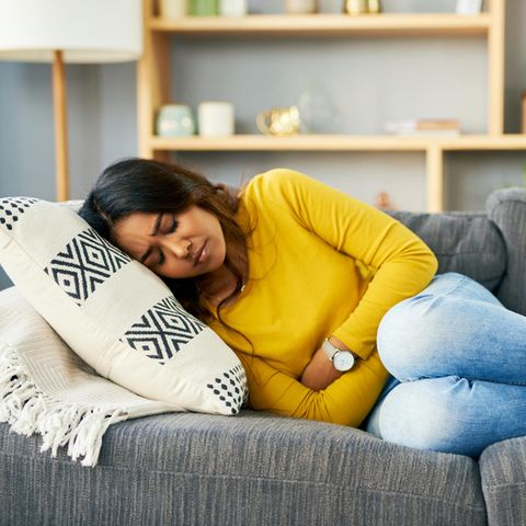 PMDS: Eine Frau liegt auf dem Sofa, hat Schmerzen und hält sich den Bauch