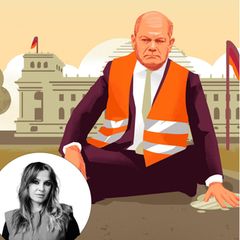 Olaf Scholz sitzt mit einer Warnweste vor dem Regierungsgebäude seine Hand klebt auf dem Boden