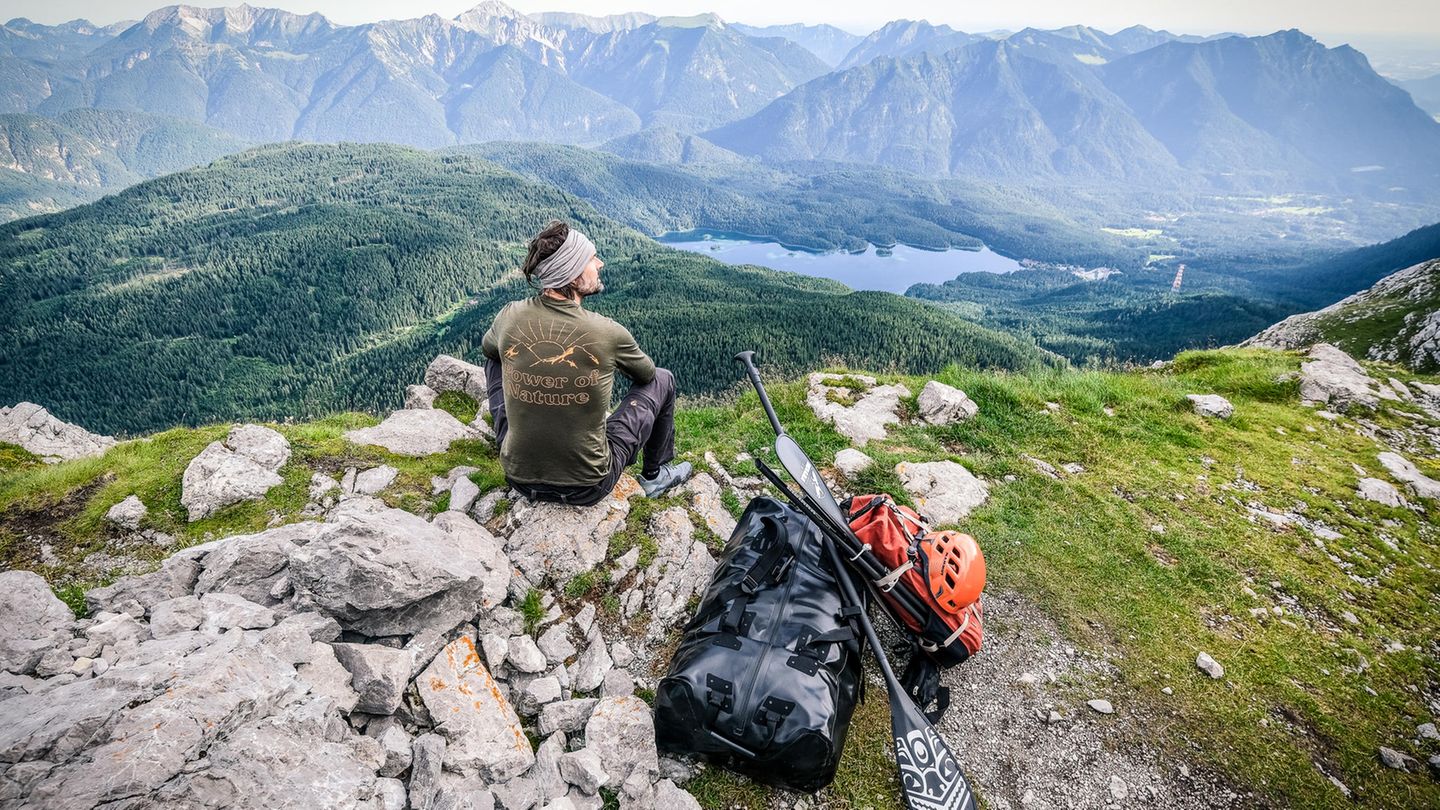 Ein Mann sitzt auf einem Felsen und schaut auf Gipfel Ein Mann sitzt auf einem Felsen und schaut auf Gipfel