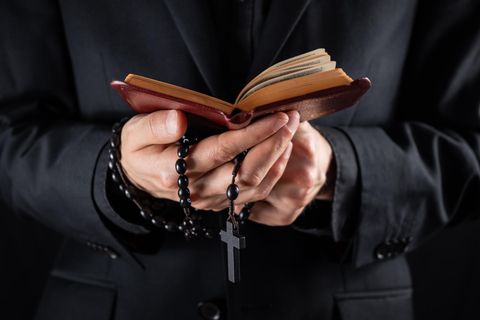 Priester mit Bibel und Kreuz