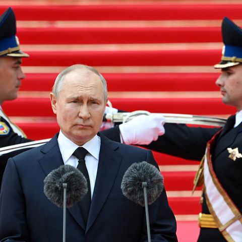 Putin steht vor einem Mikrofon, hinter ihm zwei Soldaten