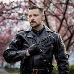 Sexarbeit: Ein Mann in Lederjacke und mit einem Lederhandschuh steht vor einem Baum