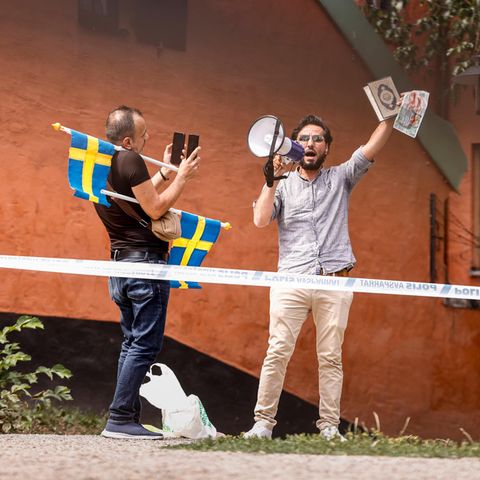 Ein nach Schweden geflüchtete Iraker hält den Koran hoch, ein weiterer Mann mit Schweden-Flaggen fotografiert ihn