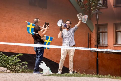 Ein nach Schweden geflüchtete Iraker hält den Koran hoch, ein weiterer Mann mit Schweden-Flaggen fotografiert ihn