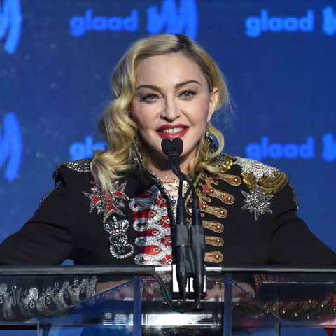 Madonna steht auf einer Bühne mit blauem Hintergrund und spricht in drei Mikrofone