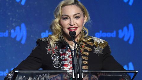 Madonna steht auf einer Bühne mit blauem Hintergrund und spricht in drei Mikrofone