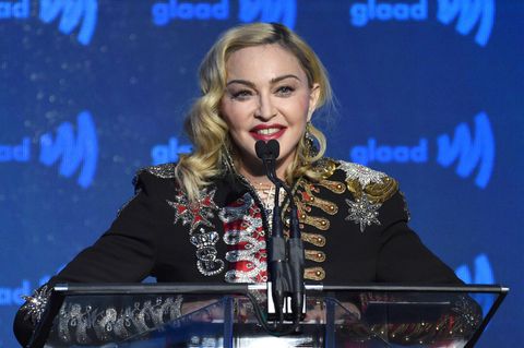 Madonna steht auf einer Bühne mit blauem Hintergrund und spricht in drei Mikrofone