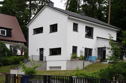 Ein weißes Haus mit asymmetrischen Fenstern steht auf einem Hanggrundstück vor einem Wald in Brandenburg