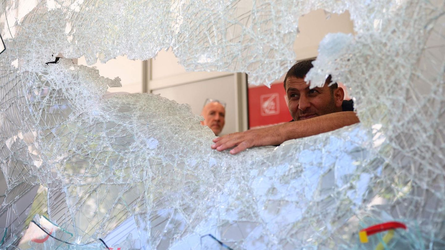 Zwei Männer untersuchen ein zerbrochenes Ladenfenster in der Stadt Marseille.