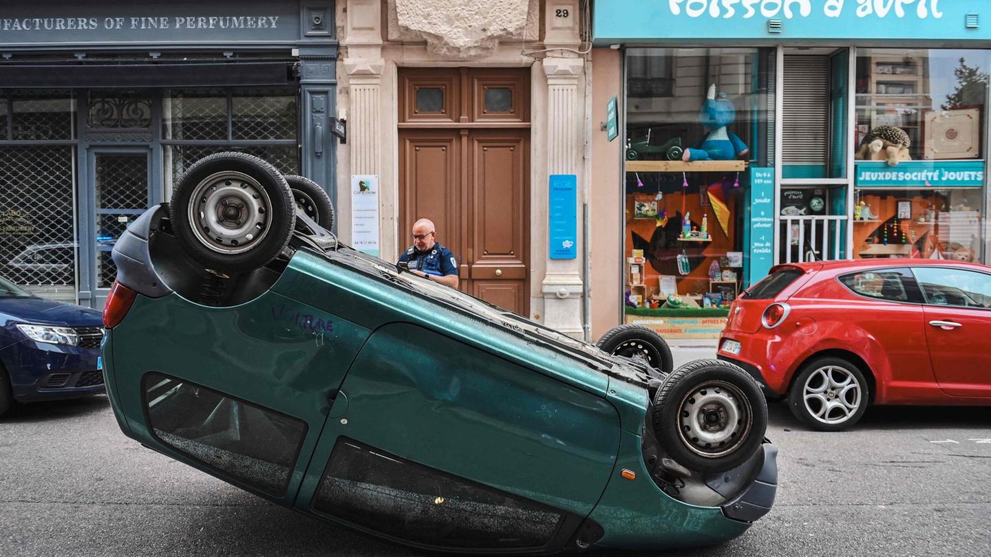 Ein Polizeibeamter inspiziert ein Auto, das in Lyon von Protestierenden auf den Kopf gestellt wurde.