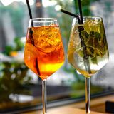 Ein Glas Aperol Spritz neben einem Glas Hugo