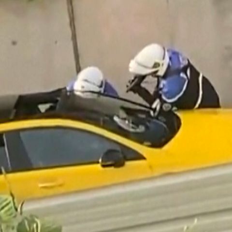 An einem gelben Auto in Frankreich stehen zwei Motorrad-Polizisten mit gezückten Waffen