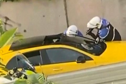 An einem gelben Auto in Frankreich stehen zwei Motorrad-Polizisten mit gezückten Waffen