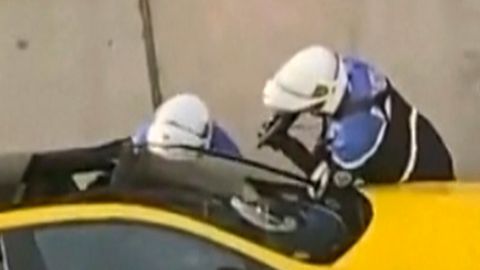 An einem gelben Auto in Frankreich stehen zwei Motorrad-Polizisten mit gezückten Waffen