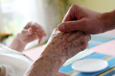 Eine junge Hand hält die einer älteren Person in einem Krankenhausbett