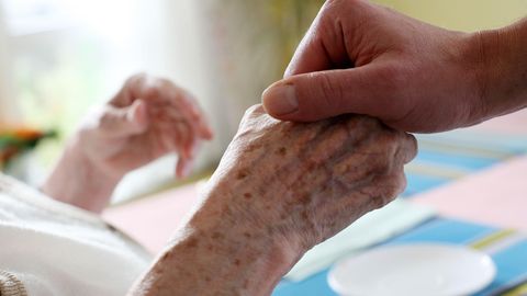 Eine junge Hand hält die einer älteren Person in einem Krankenhausbett