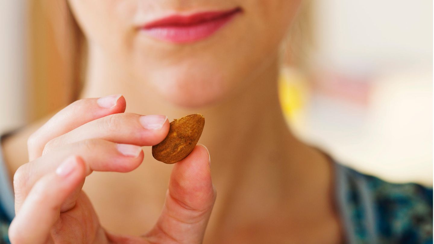 Eine Frau hält eine Mandel zwischen ihren Fingern