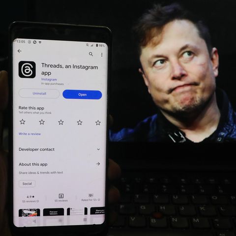Elon Musk schaut grimmig. Neben ihm ist ein Handy zu sehen mit dem neuen Angebot Threads von Konkurrent Mark Zuckerberg