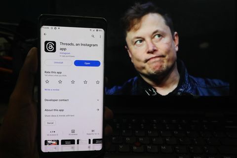 Elon Musk schaut grimmig. Neben ihm ist ein Handy zu sehen mit dem neuen Angebot Threads von Konkurrent Mark Zuckerberg